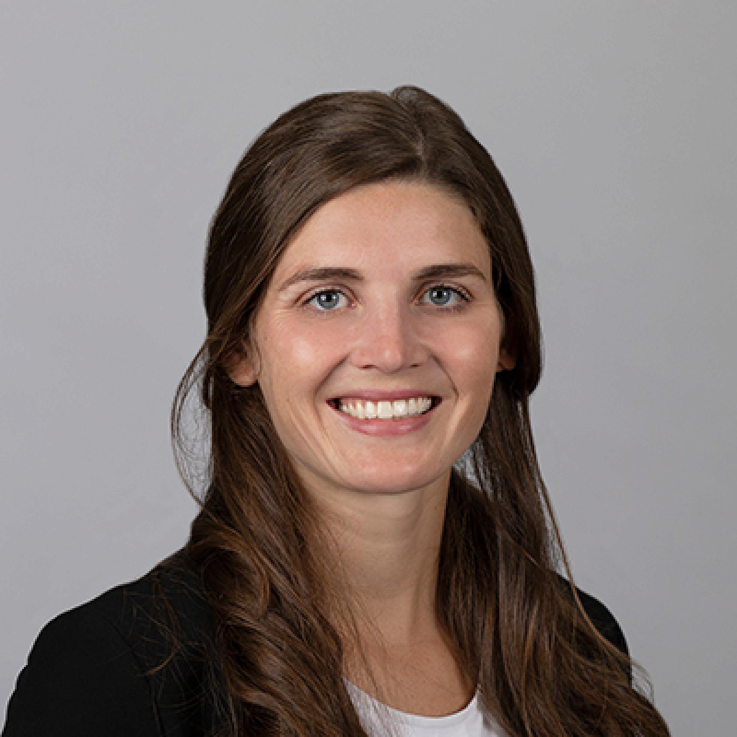 Dr. Elena Gibson's Headshot. Woman with dark brown curly hair wearing a white shirt and black blazer